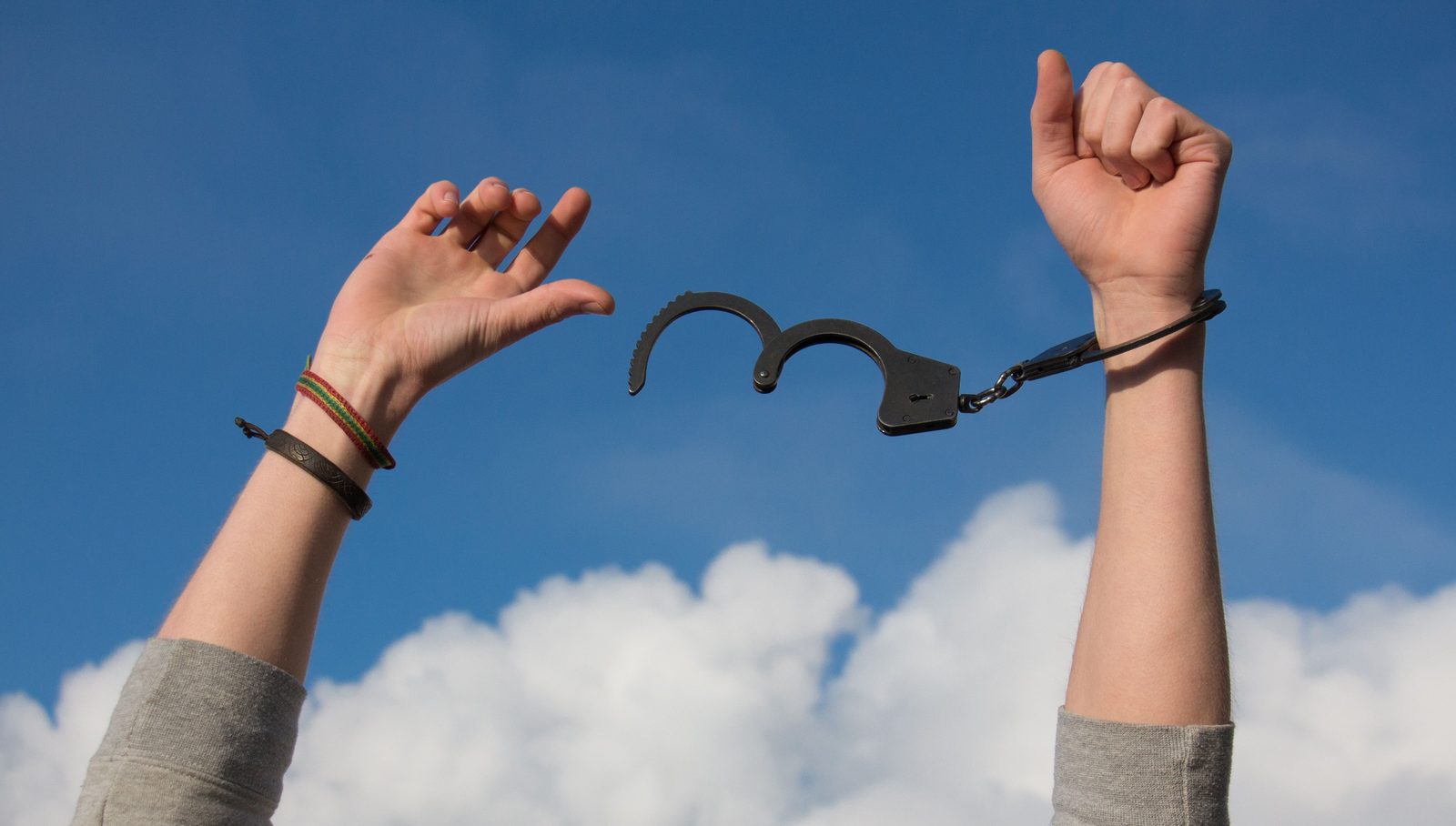 Hands breaking free against an open sky.