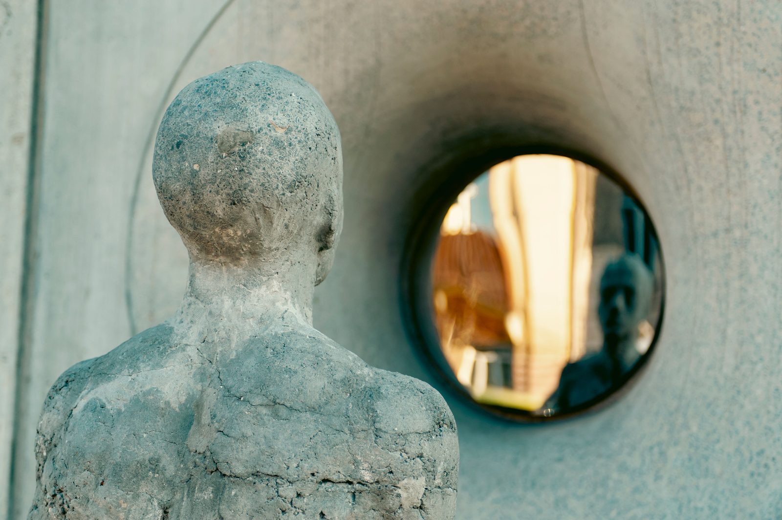 A figure turned toward its own reflection.