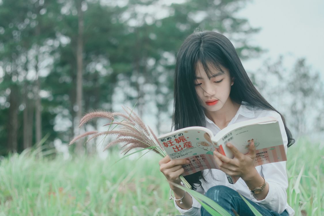 A woman reading quietly outdoors among tall grass and trees.